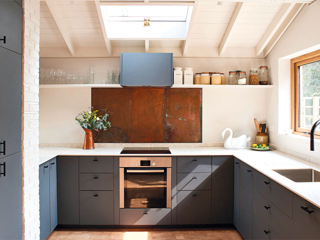 pink walled kitchen copper backsplash blue cabinets skylight above oven raised shelf with glass jars
