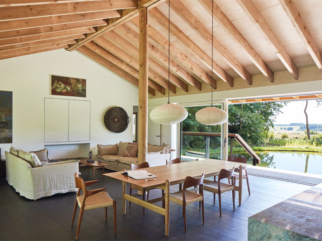 Open plan living dining area two white sofas wooden table and chairs exposed beam roof overlooking pond