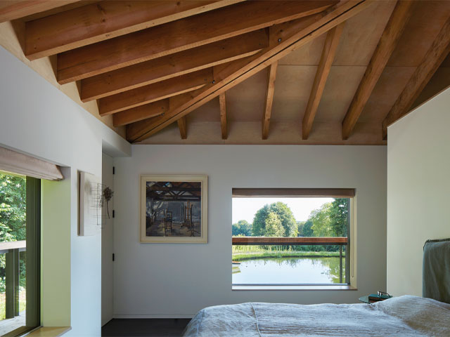 cotswolds blackbird house. exposed beam roof white bed white walls overlooking large pond