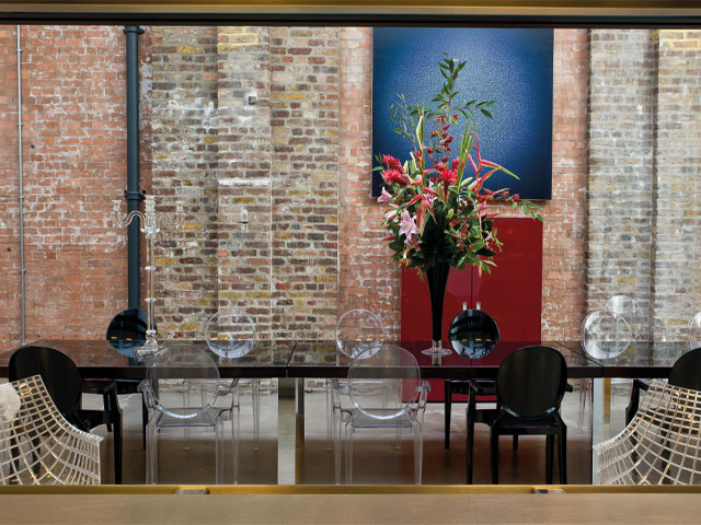 Large black dining table mismatch chairs large flower arrangement exposed brick wall 