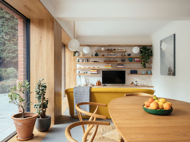 Living room with yellow sofa and large glazing wooden table with fruit bowl large pot plants
