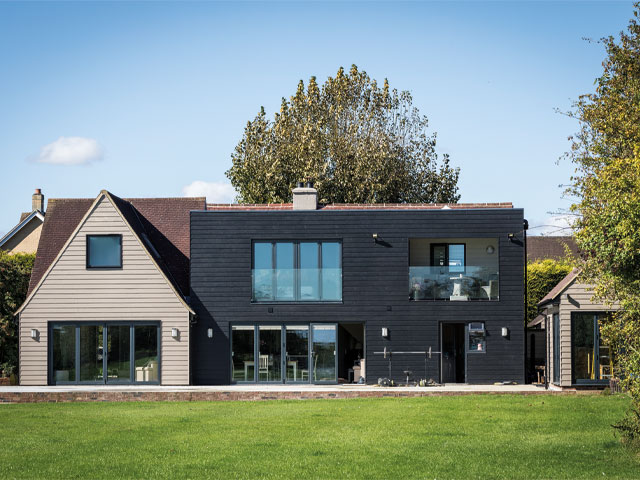 House exterior black and white with detached shed and red slate roof clear blue sky