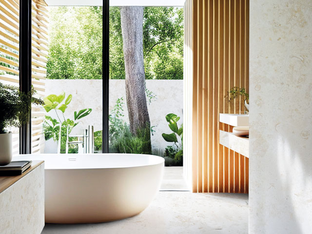 freestanding stone bath in front of patio doors glazed plants and trees 