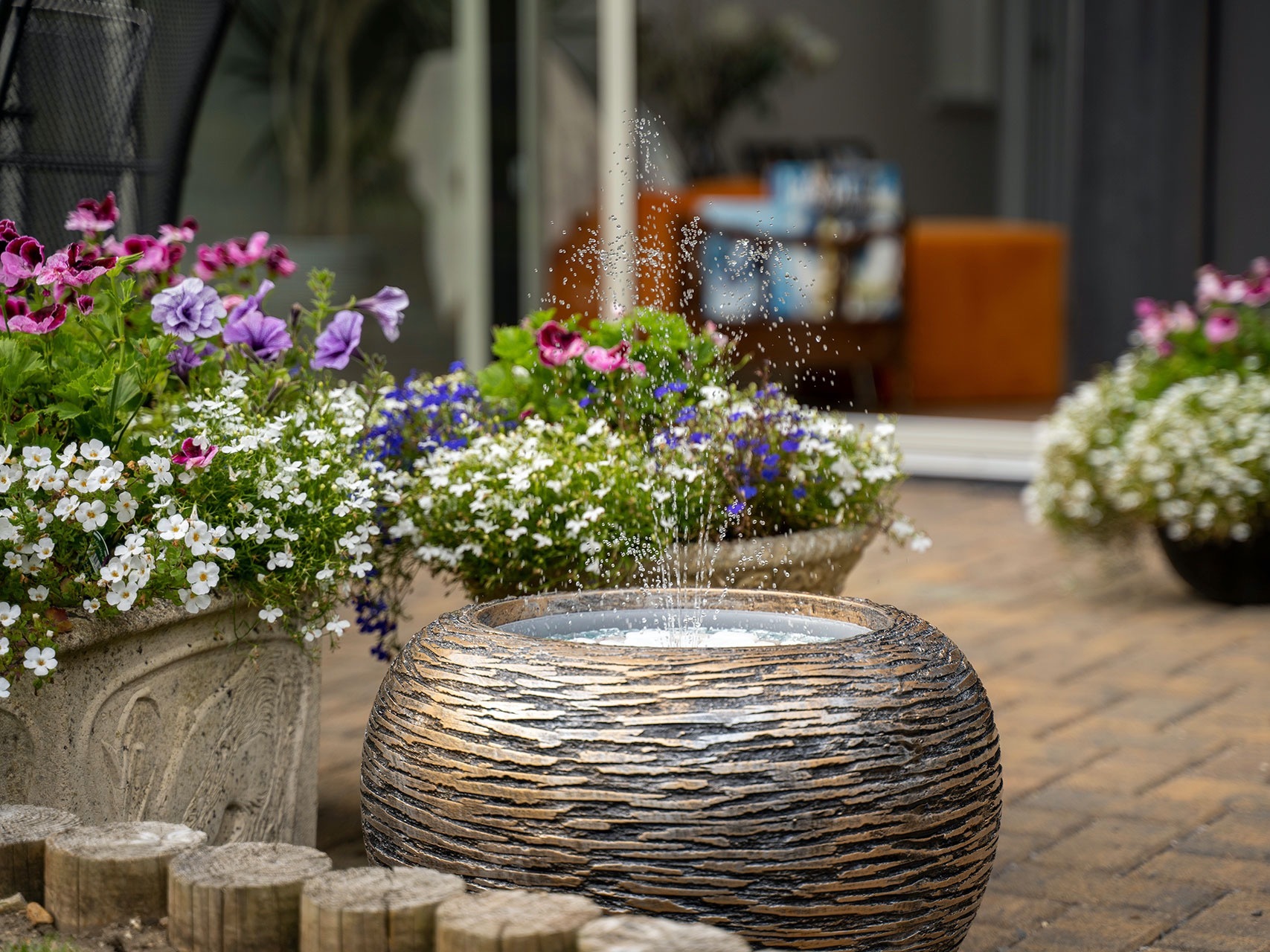 Hydria water feature next to pots of flowers