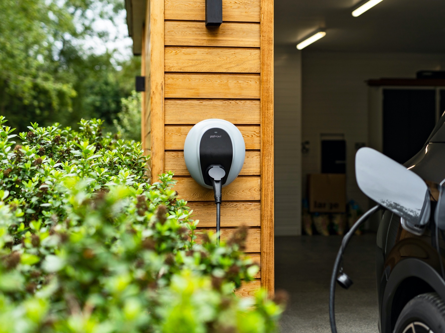 Pod Point EV car charger on timber clad garage wall