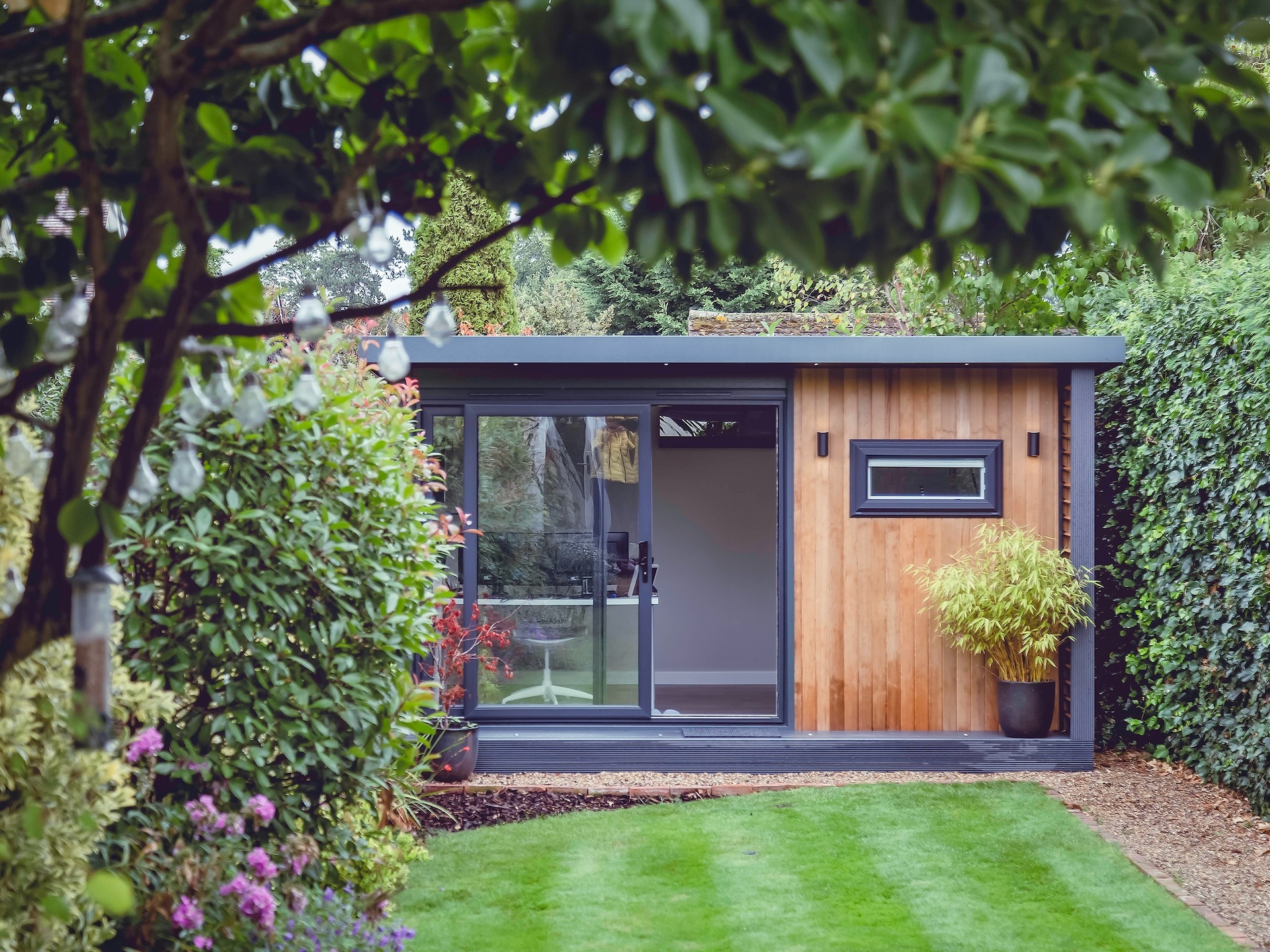 Garden room clad in wood surrounded by trees and lawn