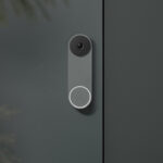 A Nest Doorbell Wired in ash, against a grey house wall