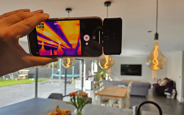 Hand holding smart device showing heat coming from infrared panels plastered into the ceiling