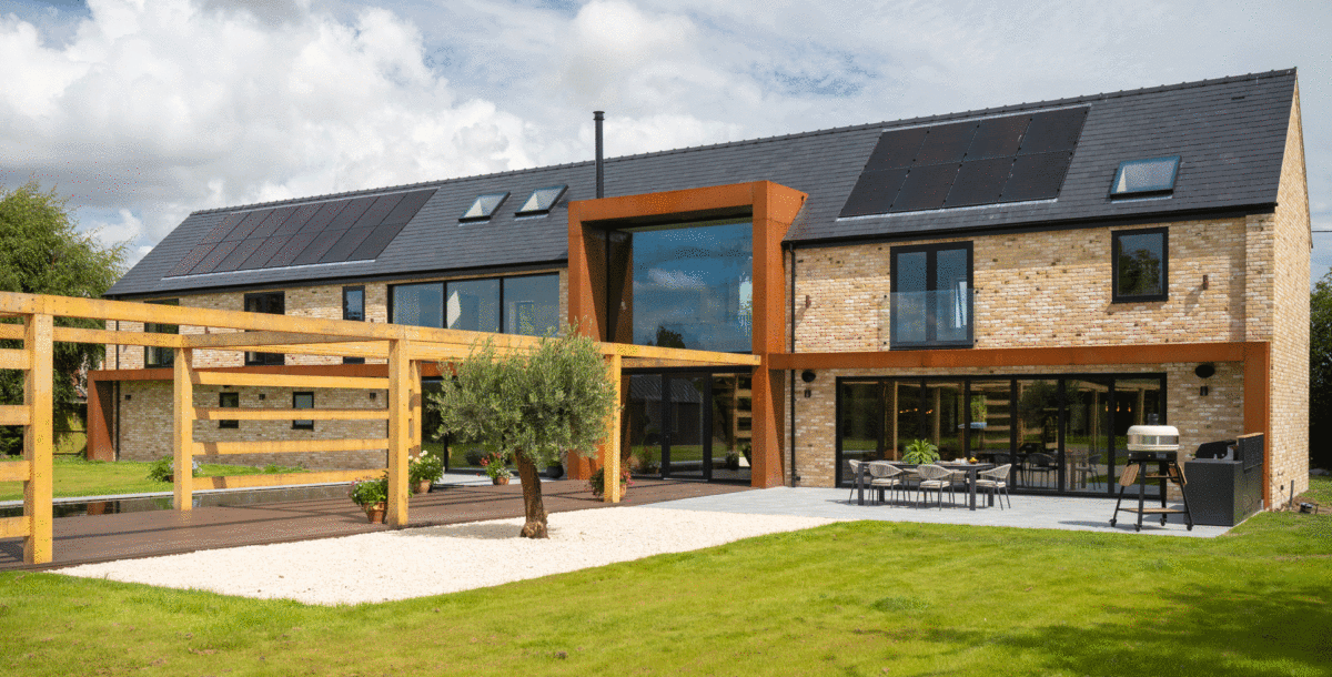 The rear exterior of a self-build brick and corten steel house with a timber pergola