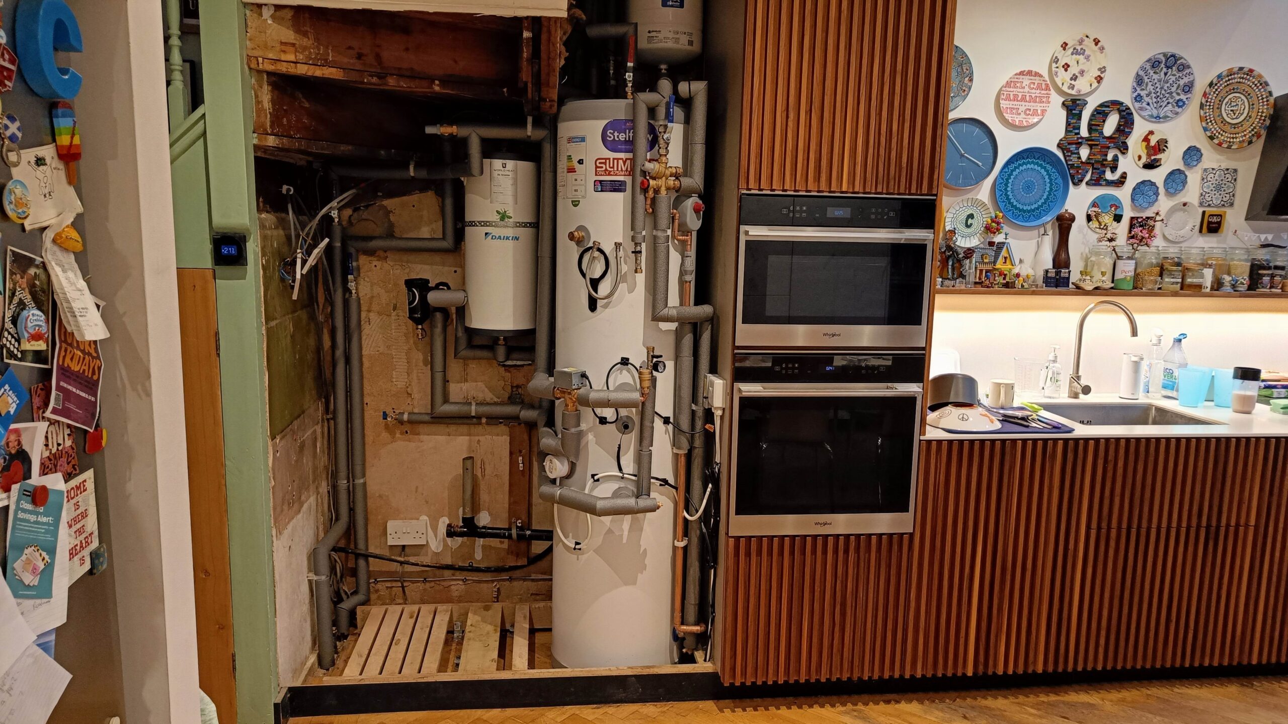 The cylinders and plumbing of an air source heat pump in a tall, walnut kitchen cabinet