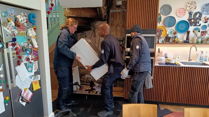 Three workers carry an old gas boiler away