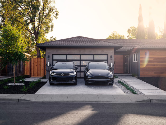 Two electric cars being charged on the driveway of a modern home