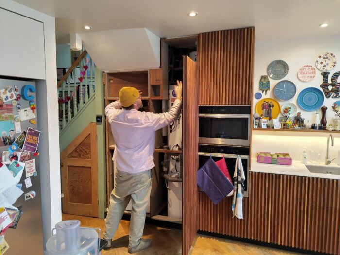 A man facing away from the camera holds his arms up, as if conducting an orchestra, while working on the kitchen cupboards.