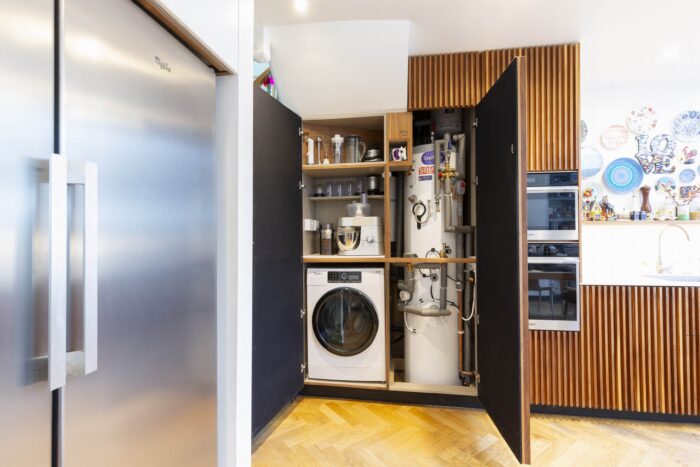 A tall kitchen cupboard containing a washing machine, some kitchen electricals and a large water tank