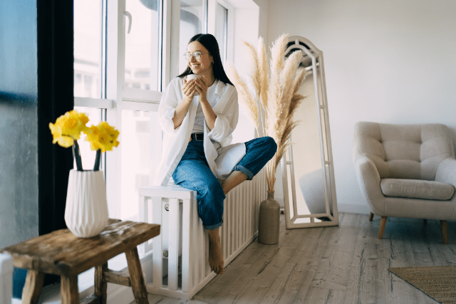 woman perching on radiator looking out window