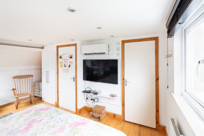 An airconditioning unit on the wall above a TV, with doors on either side
